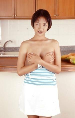 Clothed Asian with tiny tits is posing in the kitchen with spread legs on fanspics.net