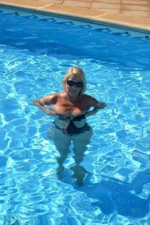 Middle-aged blonde Sweet Susi frees her tits & pussy from a swimsuit by a pool on fanspics.net