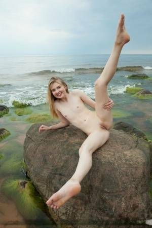 Slim teen Nimfa removes a black bikini to pose naked on seaside rocks on fanspics.net