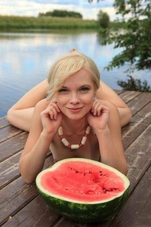 Beautiful blonde Feeona eats a watermelon while posing naked on lakeside dock on fanspics.net